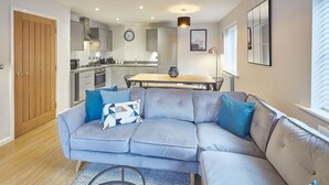 Una sala moderna con un sofá gris, una mesa de comedor y una cocina al fondo.