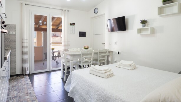 Ein Hotelzimmer mit einem Bett, einem Schreibtisch und einem Stuhl. An der Wand befindet sich ein Fernseher, eine Uhr und ein Fenster.