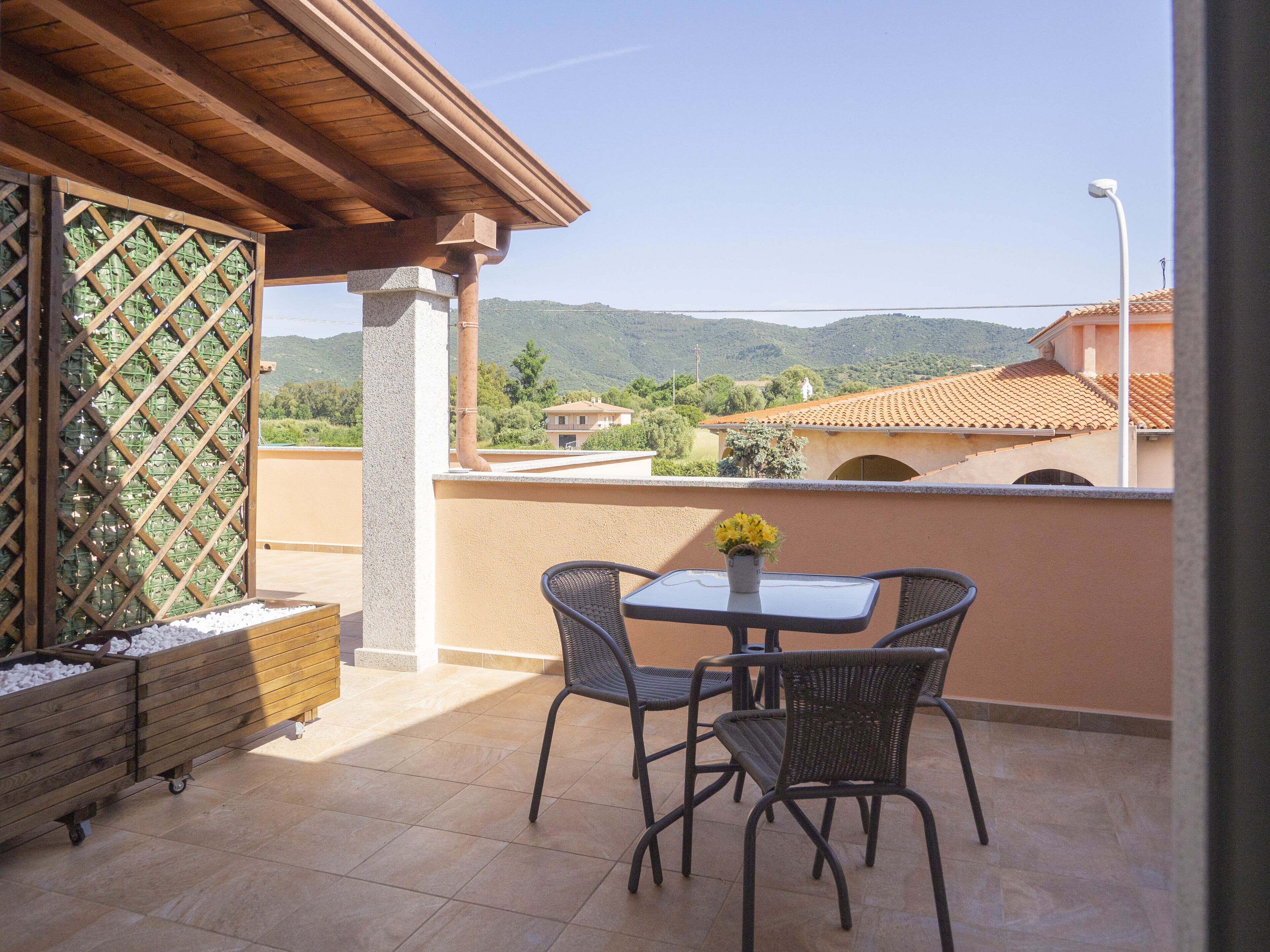 Eine Terrasse mit Tisch und Stühlen, eine Holz-Pergola und Blick auf die umliegende Landschaft.