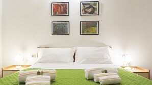 Une chambre d’hôtel avec un lit, une couvre-lit verte, des oreillers blancs et quatre œuvres d’art encadrées accrochées au mur.