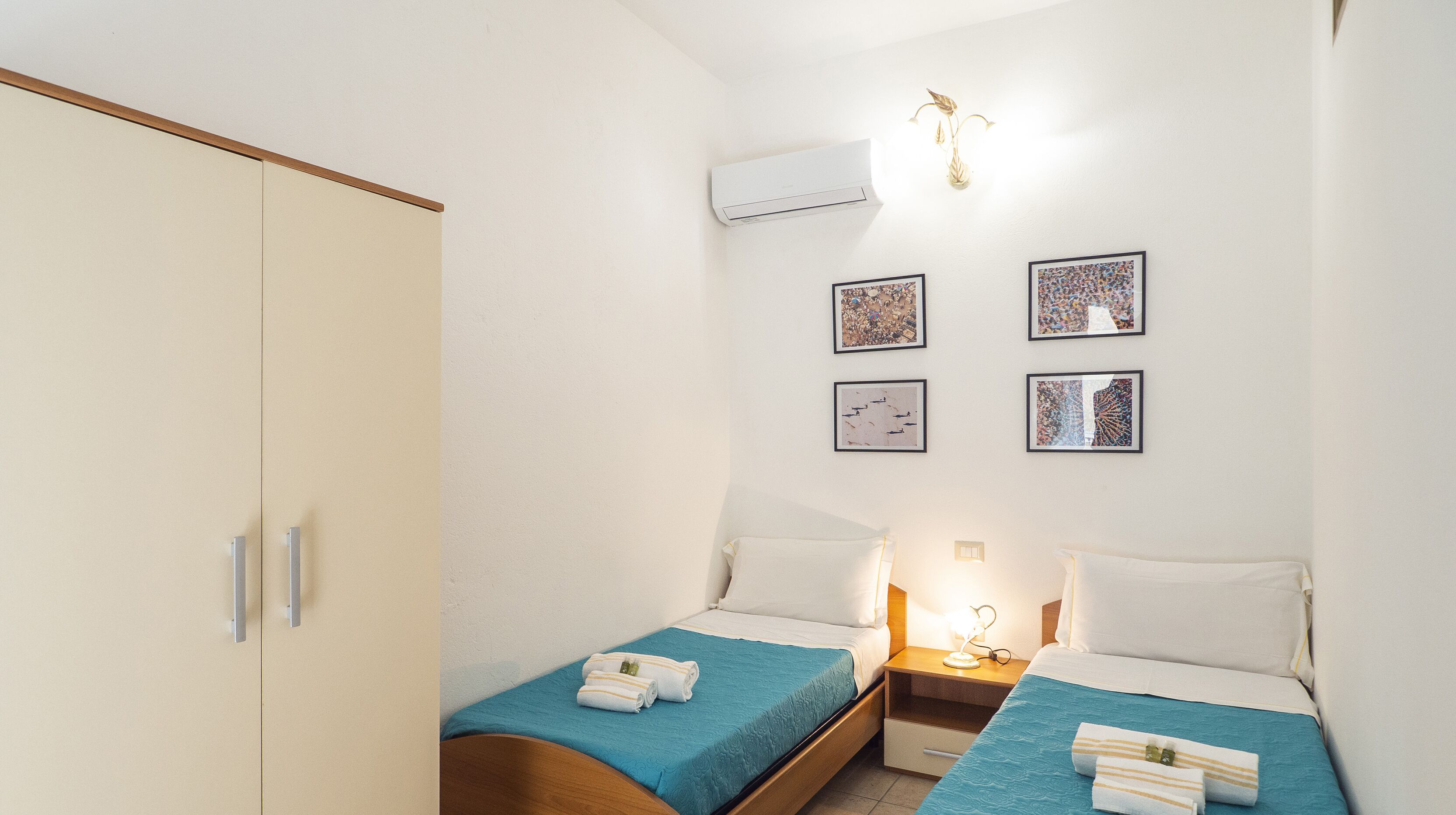 Ein Hotelzimmer mit zwei Einzelbetten, einem Kleiderschrank und vier gerahmten Kunstwerken an der Wand.