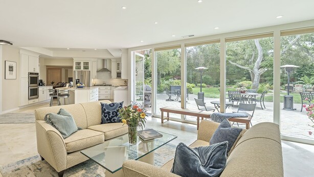 A spacious living room with a glass coffee table, beige sofas, and a view of a patio with outdoor furniture. - 3885 Pebble Beach Oasis - Indoor / Outdoor Living (Pebble Beach)