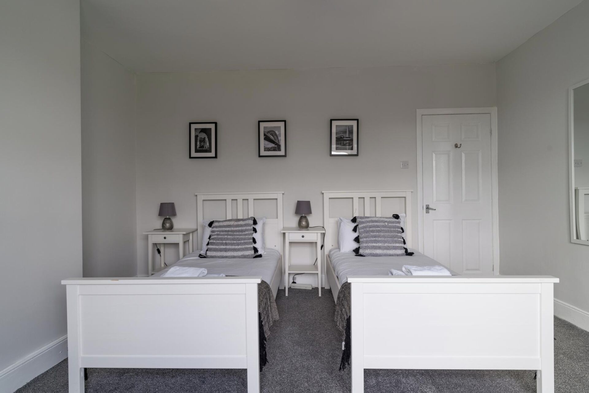 A bedroom with two single beds, a white door, and three framed pictures on the wall.