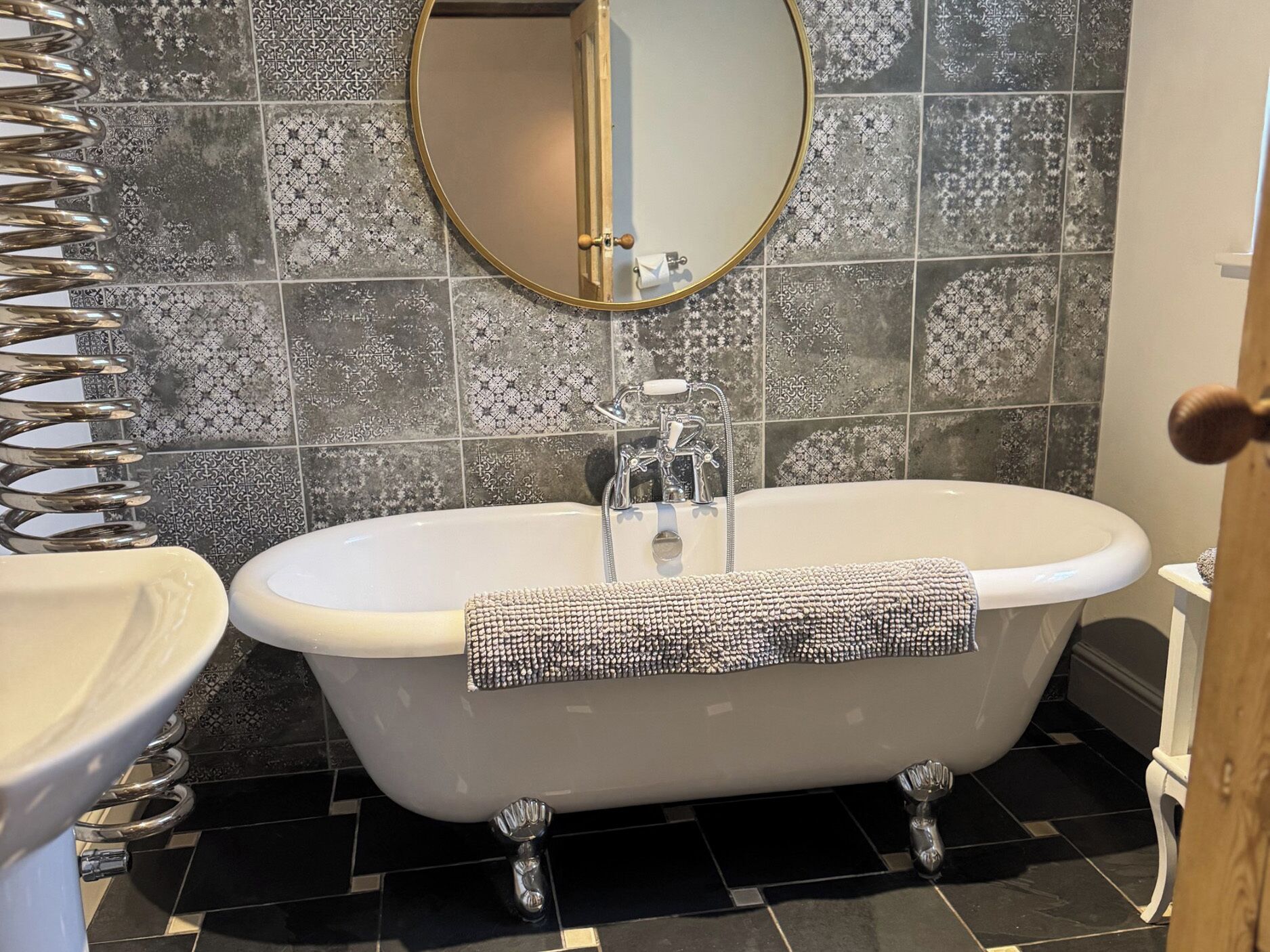 A bathroom with a freestanding bathtub, a round mirror, and a tiled backsplash.