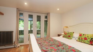 A bedroom with a bed, a radiator, a window, and a view of greenery outside. - Hillcroft (St Austell)