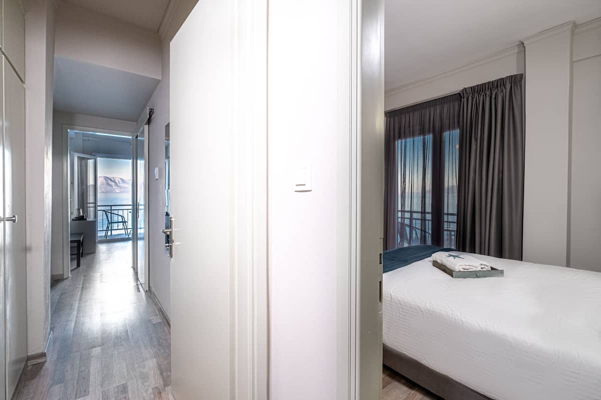 A hotel room with a bed, a window with curtains, a view of the outdoors, and a hallway leading to another room.