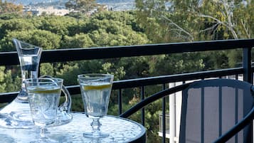 Un tavolo con tre bicchieri d'acqua e un boccale su un balcone che si affaccia su un paesaggio urbano e alberato.