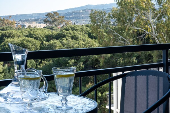 A table with three glasses of water and a pitcher on a balcony with a view of a town and trees.