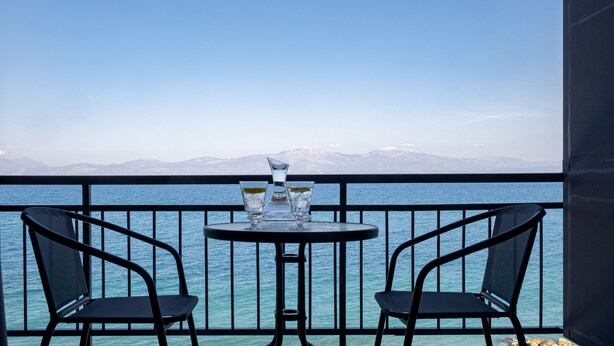A balcony with two chairs and a table, overlooking a body of water and distant mountains. - RIVIERA HOTEL (Xylokastro-Evrostina)