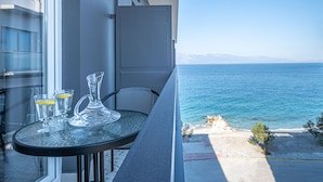 A balcony with a table, two glasses, and a glass pitcher. The view includes a body of water and distant mountains. - RIVIERA HOTEL (Xylokastro-Evrostina)
