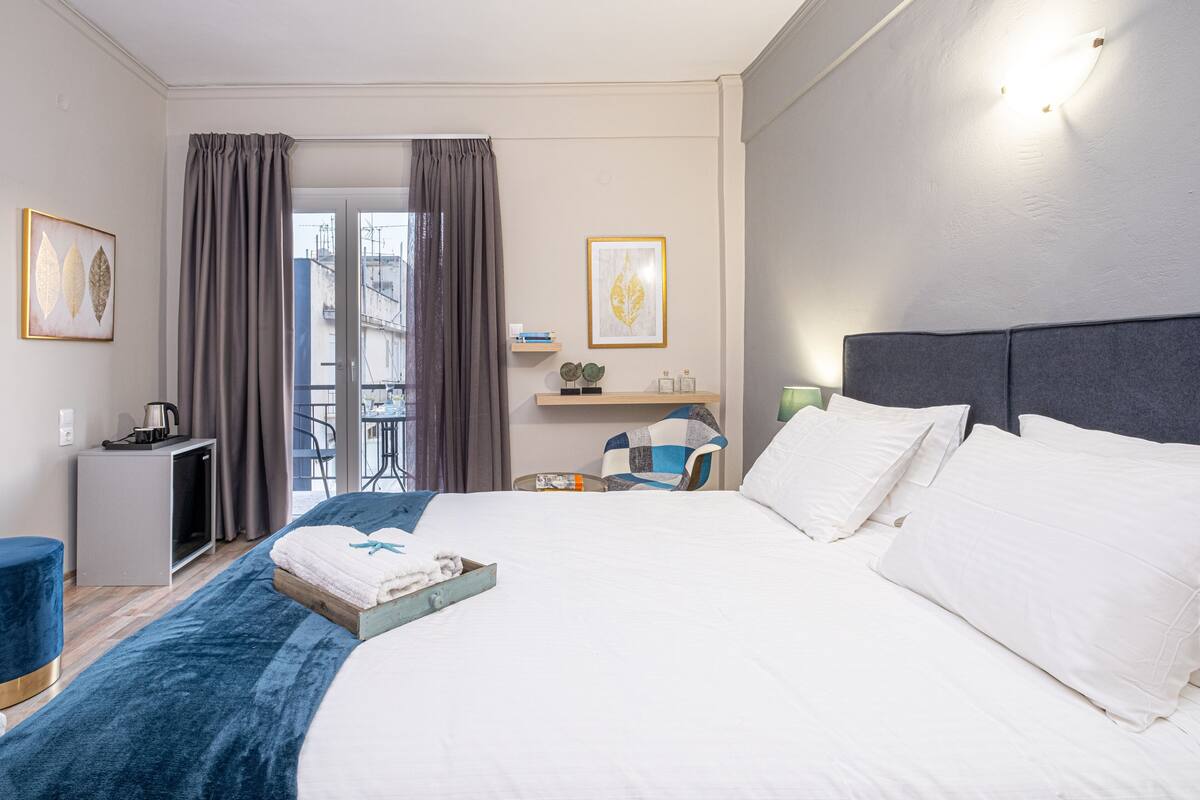 A hotel room with a large bed, a desk, a chair, a small table, and a balcony view.