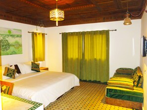 A bedroom with a large bed, two bedside tables, a green curtain, and a patterned floor. - Desert Villa Boutique Hotel Merzouga (Taouz)