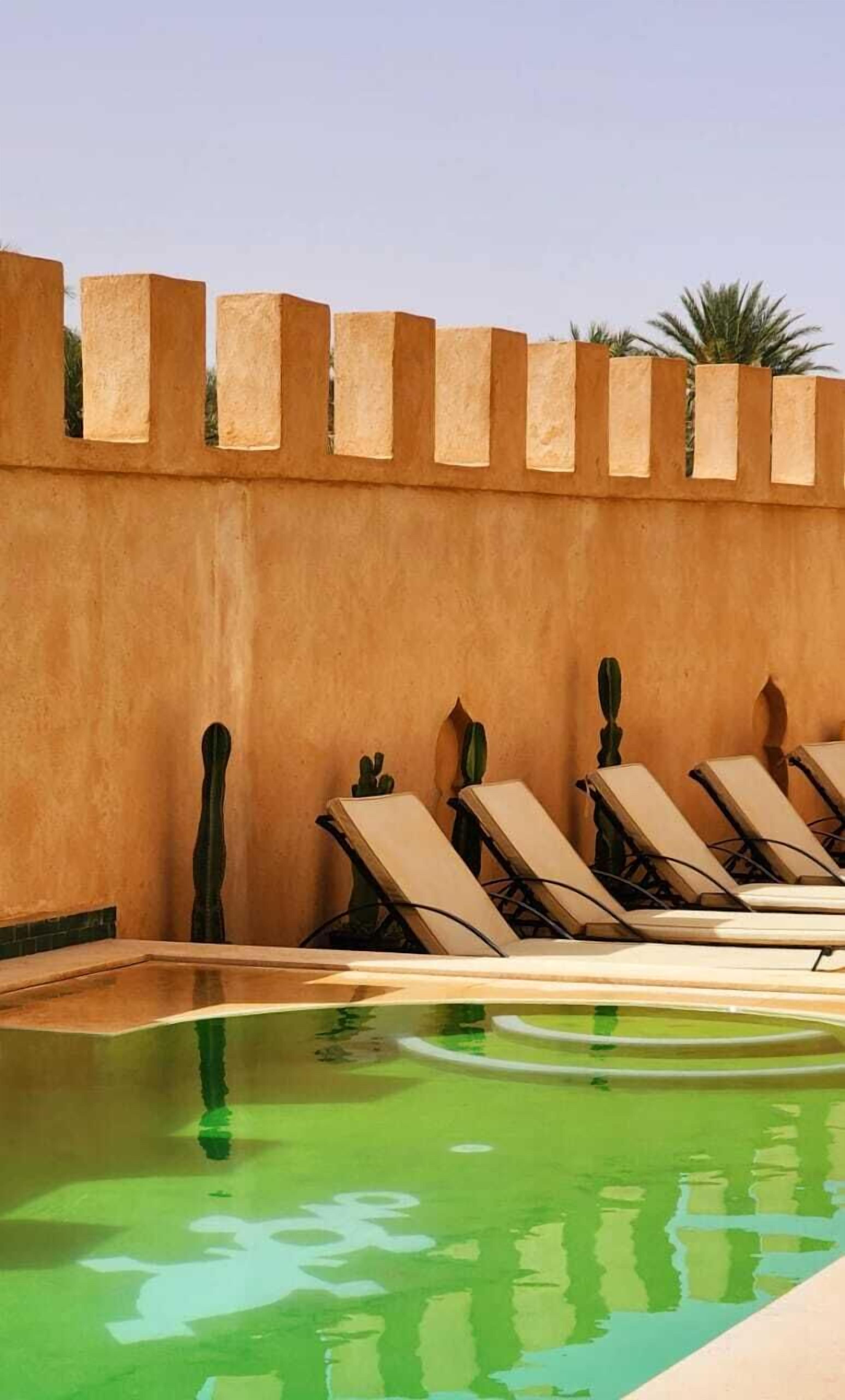 A pool area with lounge chairs and a low wall with a textured surface.