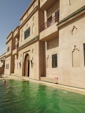 A building with a swimming pool, featuring balconies with metal railings and decorative window grills. - Desert Villa Boutique Hotel Merzouga (Taouz)