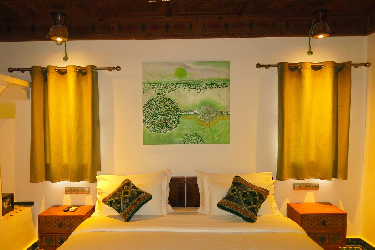A hotel room with a bed, two nightstands, a wall-mounted painting, and curtains.