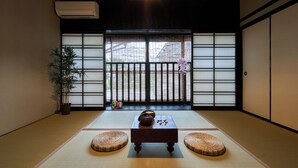 Una habitación japonesa tradicional con suelo de tatami, puertas correderas shoji, una mesa baja de tatami y una planta en maceta.