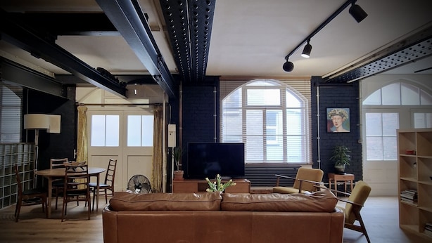 Ein modernes Wohnzimmer mit einem großen braunen Ecksofa, einem Esstisch mit Stühlen, einem Fernseher und einem Bücherregal.