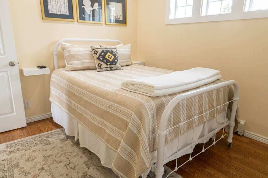 A neatly made bed with a striped bedspread, a pillow with a geometric pattern, and a white blanket folded at the foot.