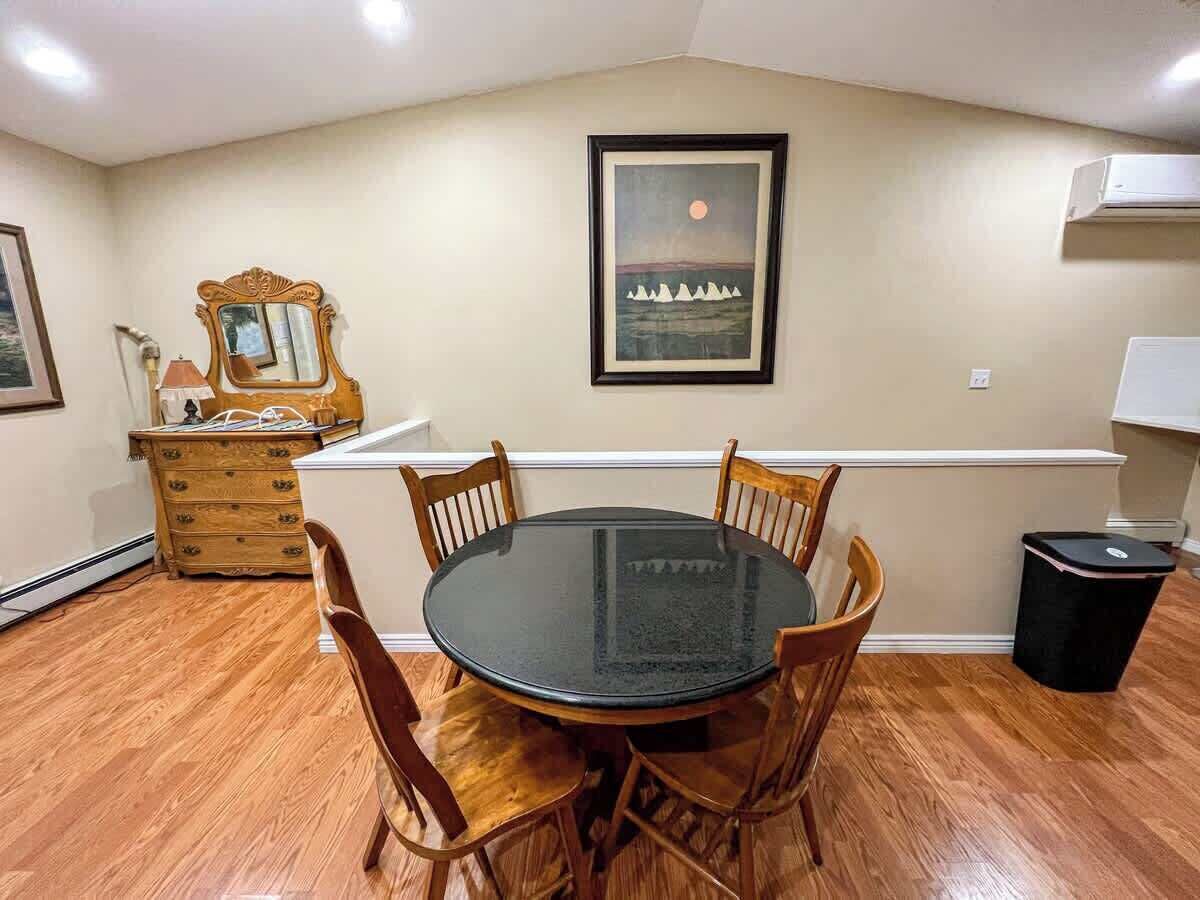 Een eethoek met een ronde glazen tafel, omringd door houten stoelen, een houten dressoir en een ingelijst schilderij aan de muur.