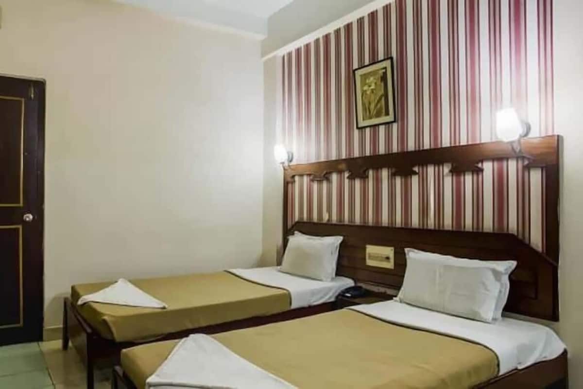 Una habitación de hotel con dos camas individuales, cabecero de madera, papel tapiz a rayas, un cuadro enmarcado y una puerta.