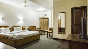 Una habitación de hotel con cama, escritorio, silla, televisor y espejo.