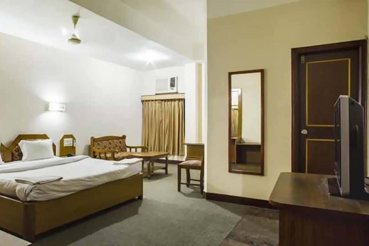 Una habitación de hotel con cama, escritorio, silla, televisor y espejo.