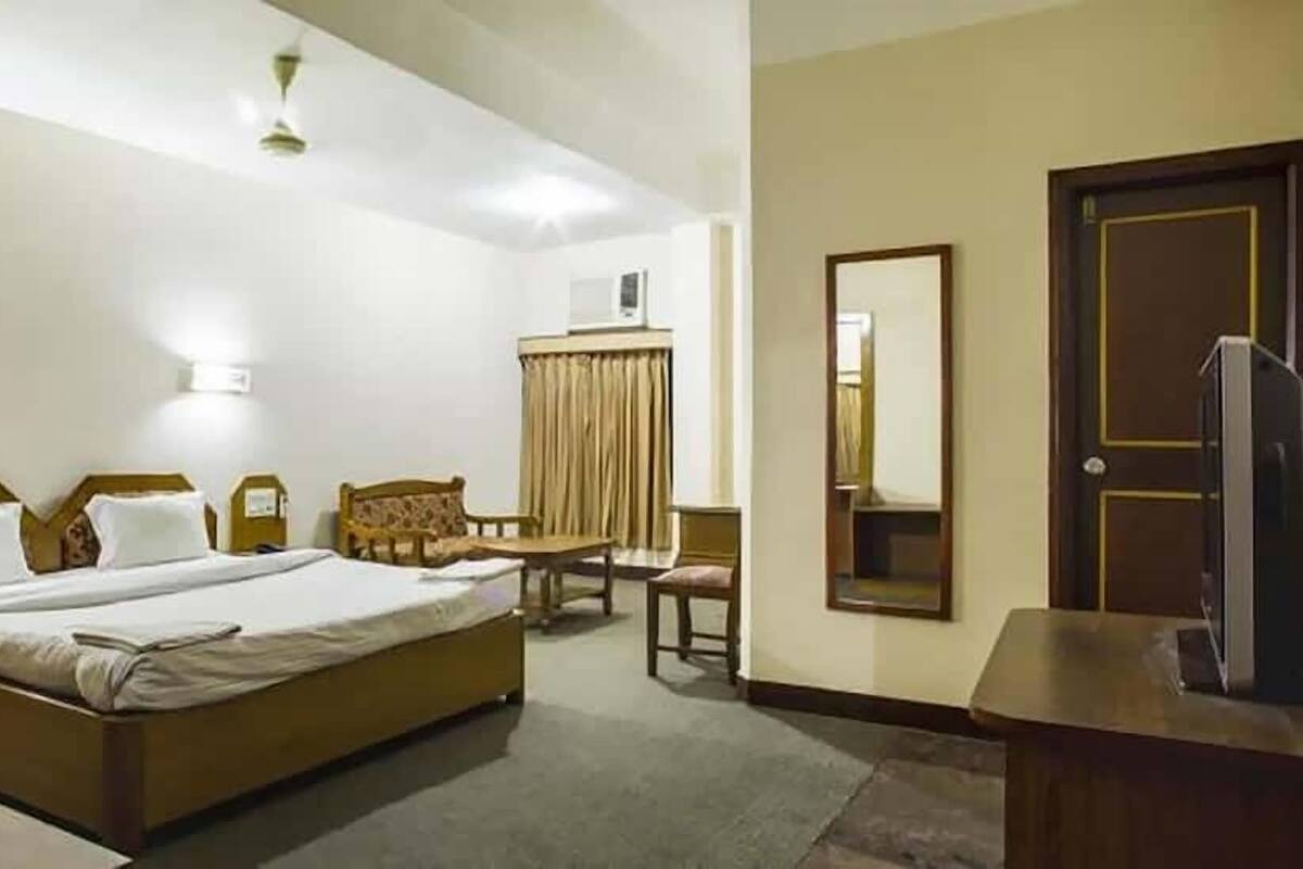 Una habitación de hotel con una cama, un escritorio, una silla, un televisor y un espejo.