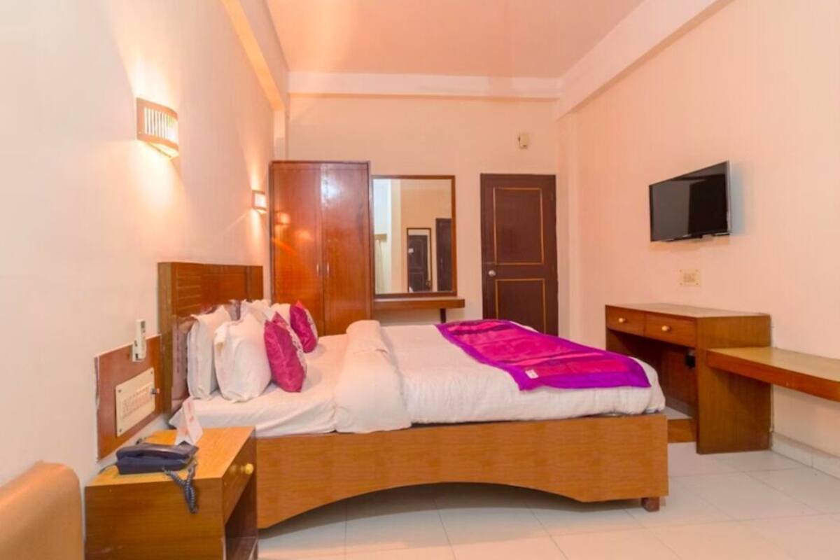 Una habitación de hotel con cama, mesita de noche, televisor y escritorio.