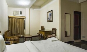 Ein Hotelzimmer mit einem Bett, einem Schreibtisch, zwei Stühlen, einem Bild an der Wand und einer Klimaanlage.