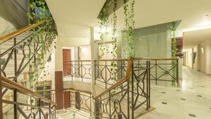 Un interior espacioso con una escalera central, barandales de metal y plantas colgantes.
