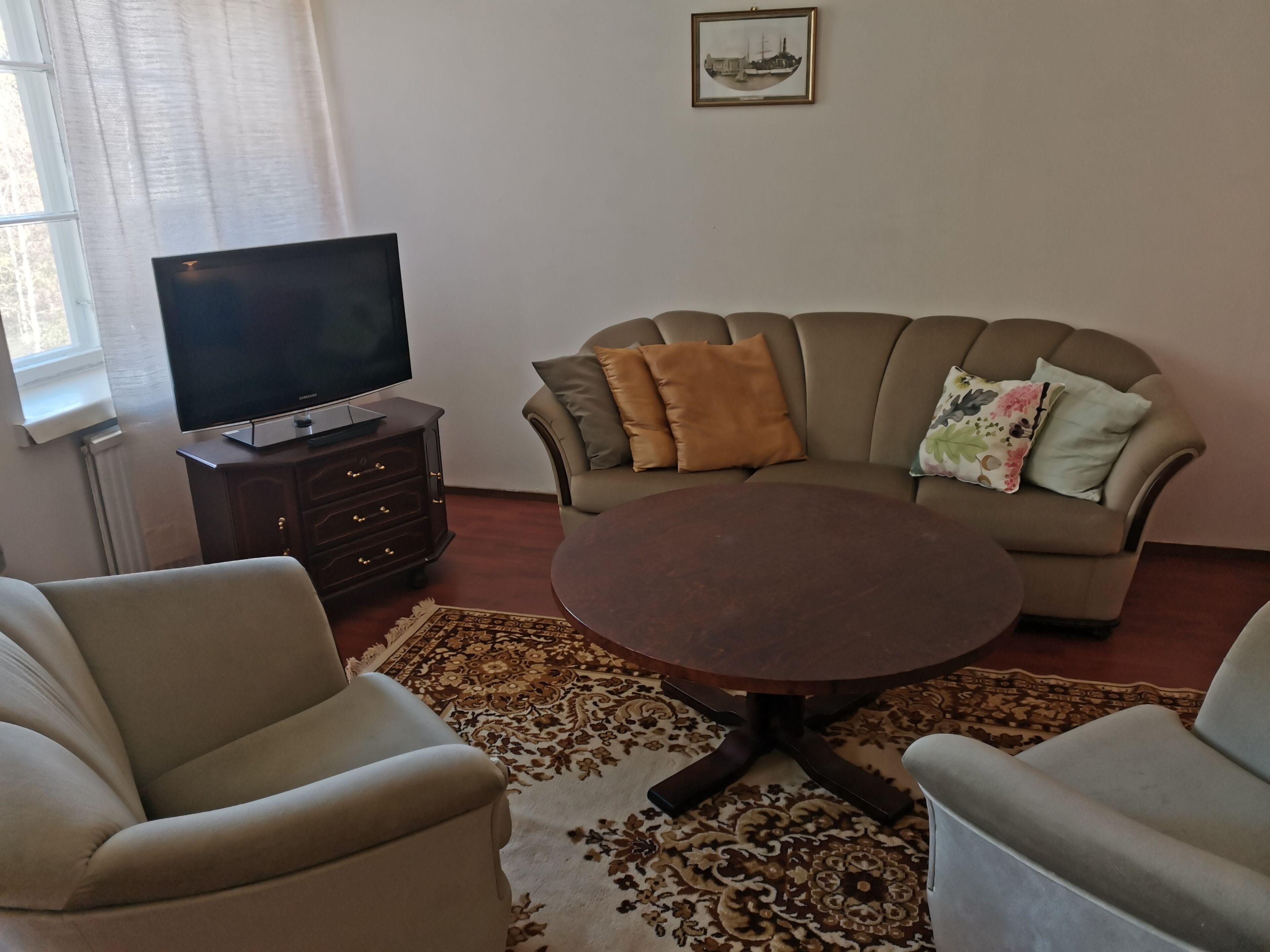 A living room with a sofa, two armchairs, a coffee table, a TV on a stand, and a patterned rug.
