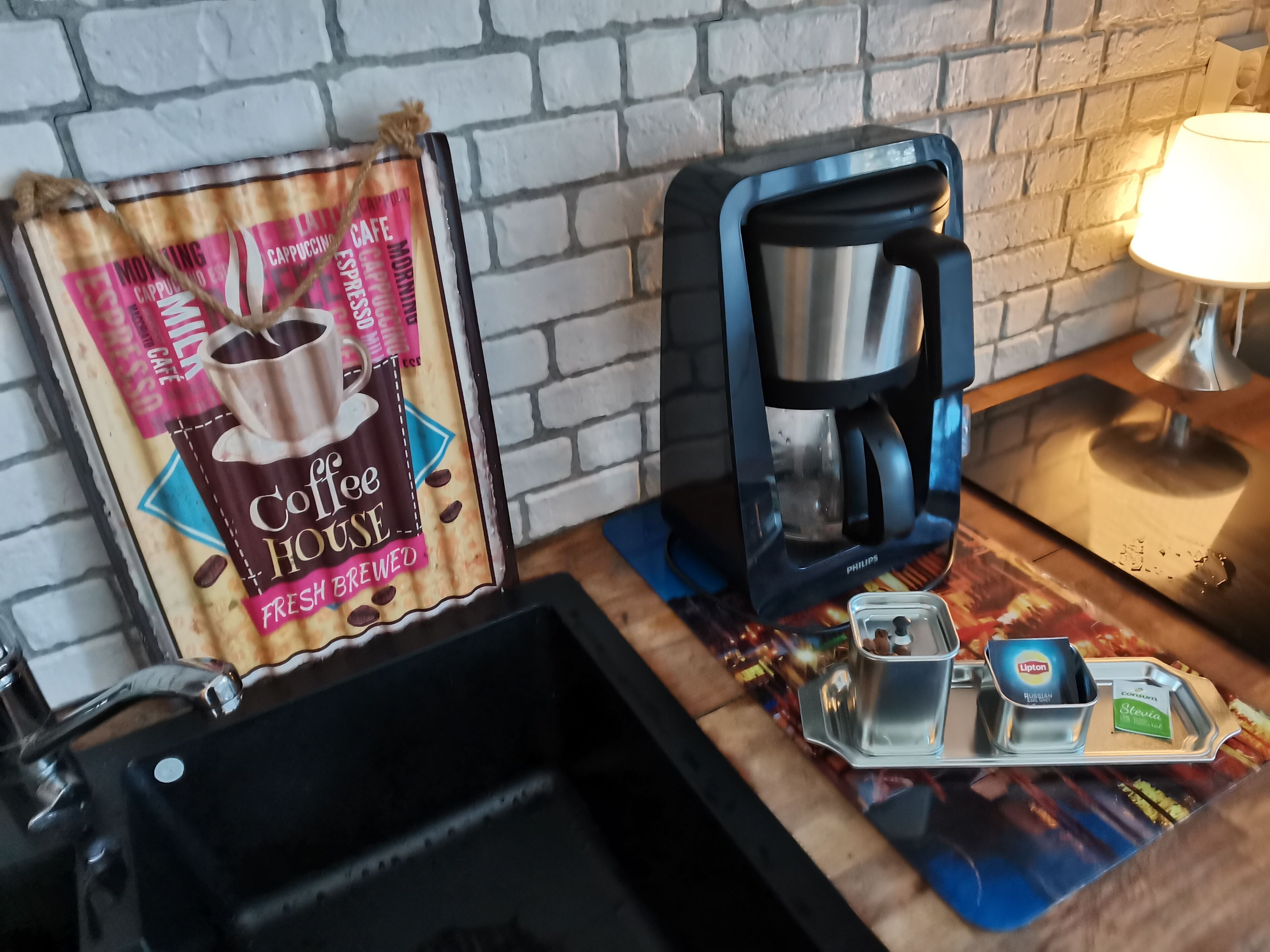 Kahvinurkkaus, jossa on kahvinkeitin, alusta kahvikapseleille ja kahvipussi, jonka etiketissä lukee: ”The Coffee House – tuoretta, juuri haudutettua kahvia”.