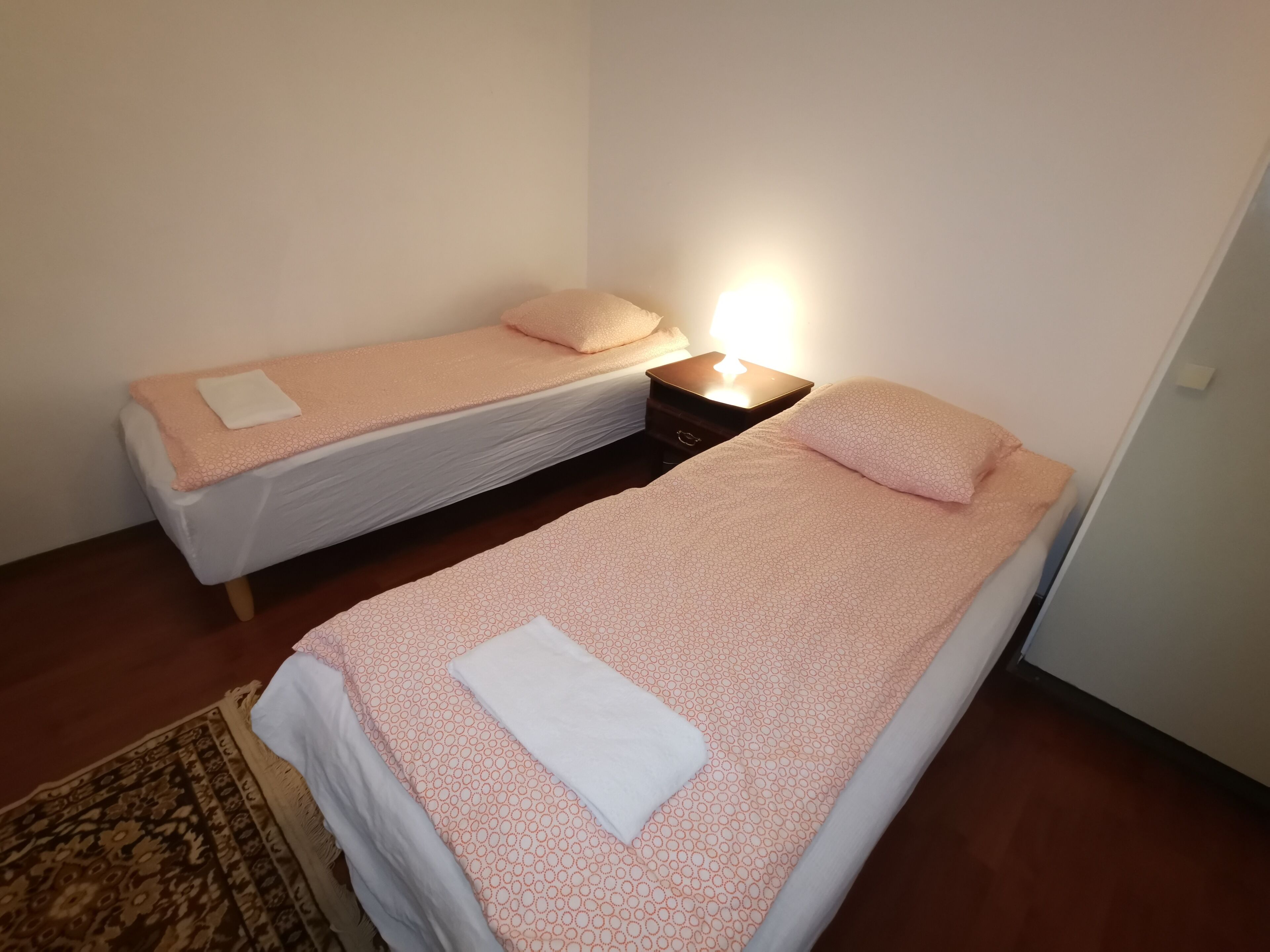 A room with two single beds, each with a matching pillow and a bedside table with a lamp.
