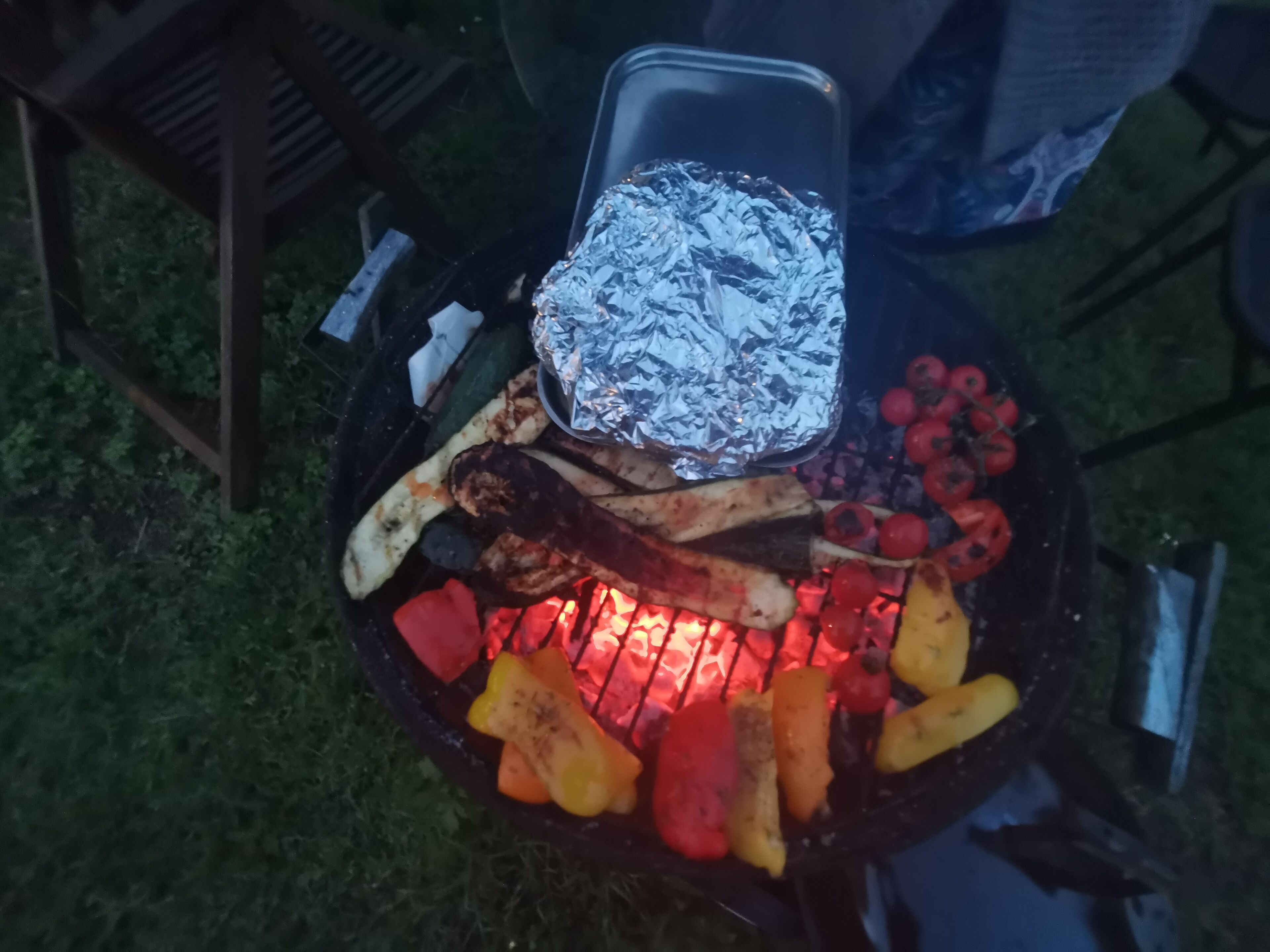 A grill with various vegetables and meat, surrounded by a wooden fence and greenery.