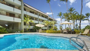 A swimming pool with a stone deck, surrounded by palm trees and lounge chairs. - Summer Deal Kona 2BR Condo Across Magic Sands Beach with Ocean Views (Kailua Kona)