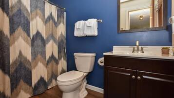 Une salle de bain avec des toilettes blanches, un mur bleu, un meuble en bois foncé et un rideau de douche à motifs géométriques.
