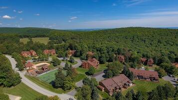 An aerial view of a residential area with multiple brick houses, green lawns, and a tennis court.