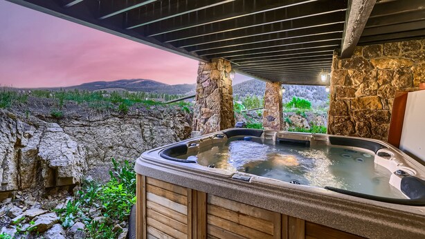 A hot tub under a stone structure with a view of a mountainous landscape.