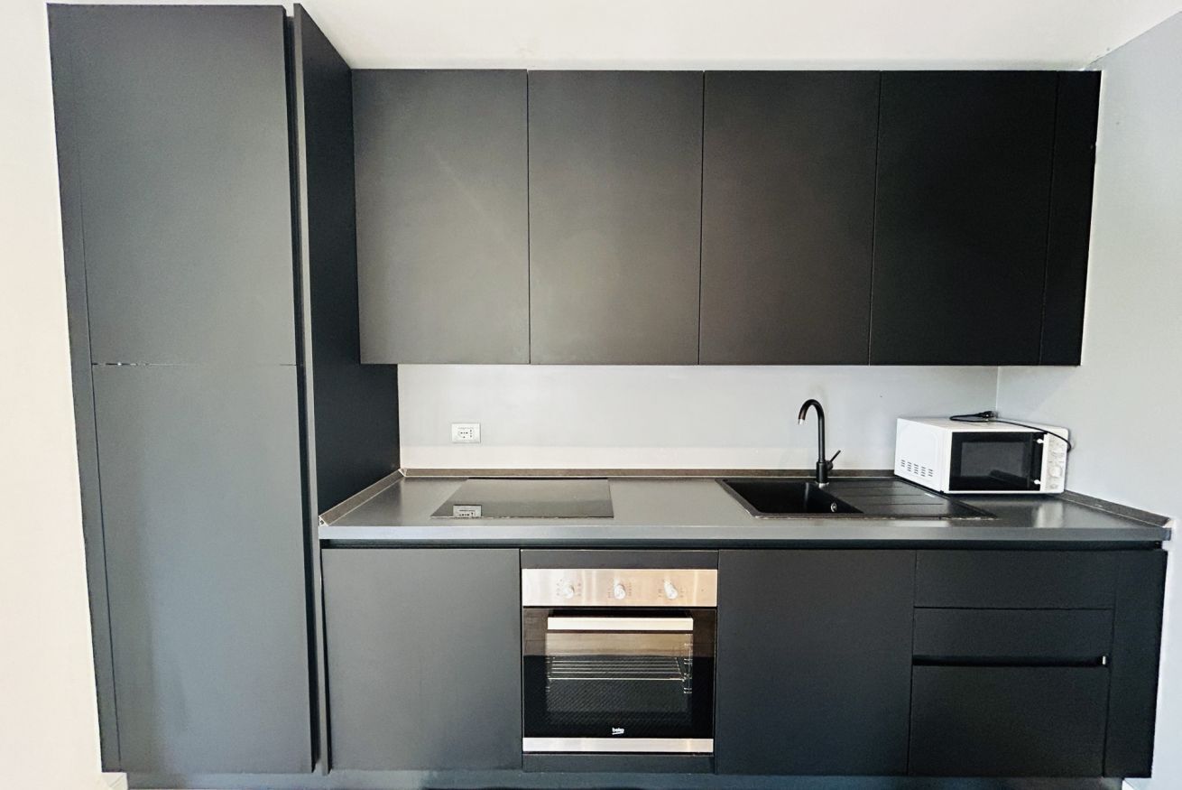 Een moderne keuken met donkere kastjes, een inbouwoven, een magnetron en een spoelbak.