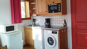 Una cocina compacta con armarios de madera, un microondas, una cafetera y una lavadora.