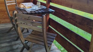 Terraza de madera con una mesa y sillas, con vista a un valle boscoso.