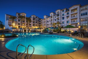 A hotel with a large swimming pool, multiple balconies, and outdoor seating areas.