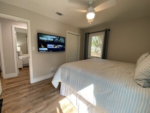 A bedroom with a bed, a ceiling fan, a TV on the wall, and a window with curtains.
