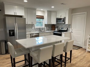 A modern kitchen with white cabinetry, stainless steel appliances, a central island with bar stools, and a window with a view.