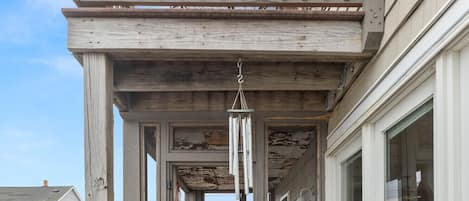 A wooden deck with a railing, a hanging wind chime, and a view of a neighboring house.