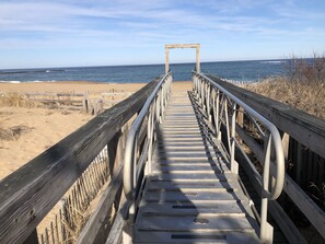 En träpromenad som leder till en strand, med ett metallräcke och en träbåge i slutet.