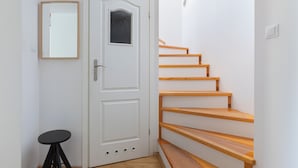 Une porte blanche avec une petite fenêtre, un escalier en bois et un tabouret noir.