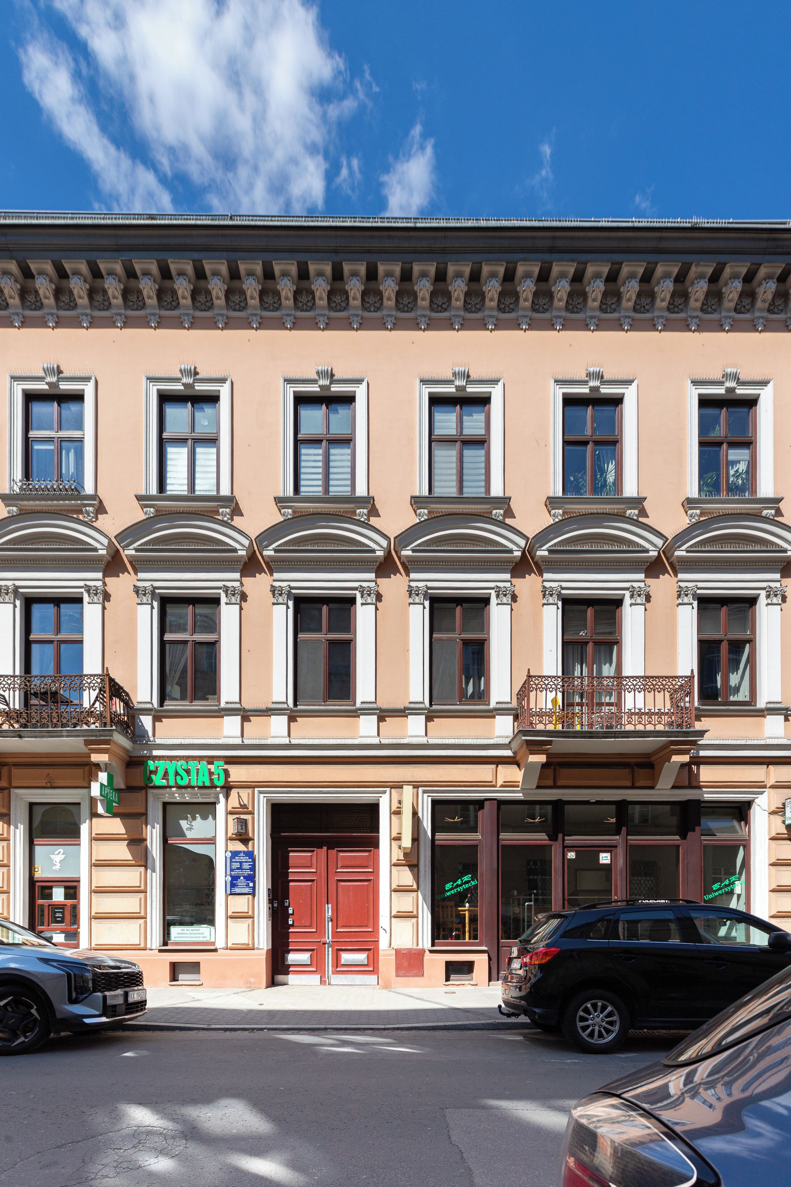A multi-story building with a row of windows, a red door, and a sign that reads 'CZYSTA 5'.