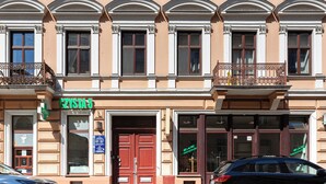 Un immeuble à plusieurs étages, avec une rangée de fenêtres, une porte rouge et une enseigne sur laquelle on peut lire « CZYSTA 5 ».
