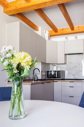 A modern kitchen with white cabinets, a microwave, and a vase with flowers on the table.